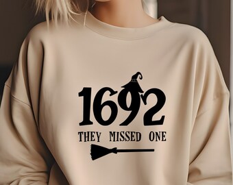 May include: A beige sweatshirt with a black graphic print that says "1692 They Missed One" with a witch's hat and broom.