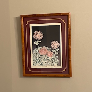 May include: Framed floral art print featuring pink and red flowers with green leaves against a dark background. The print is set within a burgundy mat and a bamboo-style wooden frame, adding a touch of nature-inspired decor.
