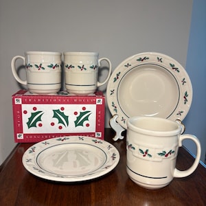 May include: A set of cream-colored ceramic dinnerware featuring a holly leaf and berry pattern. The collection includes three mugs, one small plate, and one bowl, all displayed with a red and white box labeled Traditional Holly Longaberger Pottery.