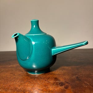 May include: A teal ceramic teapot with a rounded body and a long, thin spout. The teapot has a simple, elegant design.