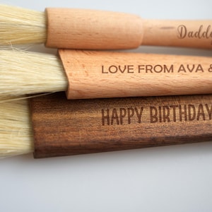 May include: Three wooden pastry brushes with natural bristles. The top brush has the text "Daddy's Bakery" engraved on the handle. The middle brush has the text "Love from Ava & Ryan" engraved on the handle. The bottom brush has the text "Happy Birthday Mom" engraved on the handle.