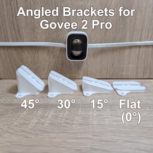 May include: Four white angled brackets for Govee 2 Pro, labeled 45°, 30°, 15°, and Flat (0°). The brackets are arranged in a row, showing varying slopes for mounting. A Govee 2 Pro light unit is visible above the brackets with a white power cable.