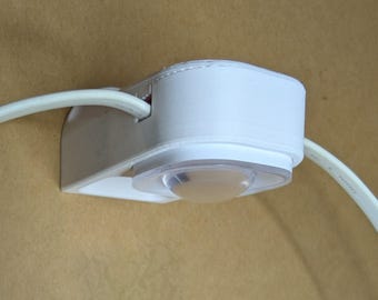 Op de afbeelding: Een witte plastic kabelorganizer met een helder, afgerond licht. De organizer heeft een gebogen ontwerp en houdt een witte kabel vast. Het item is gemonteerd op een lichtbruin oppervlak.