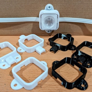 May include: A clear, square LED light fixture is mounted with screws. Below are six 3D-printed mounting brackets: three white and three black. The brackets have a square frame with a tab and mounting holes.