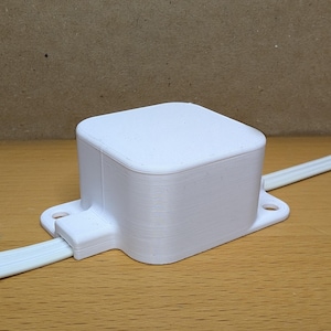 May include: A white plastic box with a cable attached to it. The box has a smooth, matte finish.