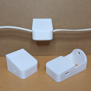 Może przedstawiać: Trzy białe plastikowe organizery do kabli. Jeden jest przymocowany do białego kabla, a dwa są oddzielne. Organizery są prostokątne z lekko pochyloną górą i małą szczeliną lub otworem.