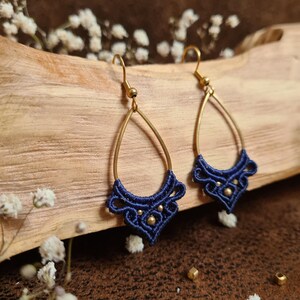 Könnte beinhalten: Ein Paar blaue und goldene Ohrringe mit einem zarten, filigranen Design. Die Ohrringe sind aus einem blauen Band und goldenen Perlen gefertigt und hängen an goldenen Haken.