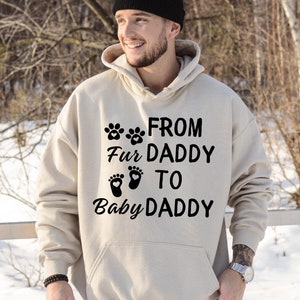 May include: A beige hoodie with a black print that reads "From Fur Daddy to Baby Daddy" with paw prints and footprints.