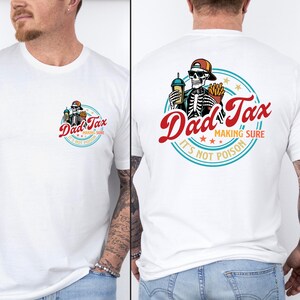 May include: White t-shirt featuring a graphic of a skeleton wearing a cap and sunglasses, holding a drink and fries, with the text "Dad Tax" in red and "Making Sure It's Not Poison" in a circular design. The shirt is short-sleeved.