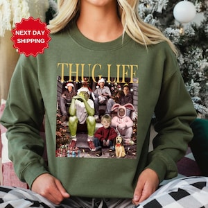 May include: Green sweatshirt with a Christmas-themed graphic featuring the characters from the movie 'Home Alone' with the text 'THUG LIFE' printed in gold letters.