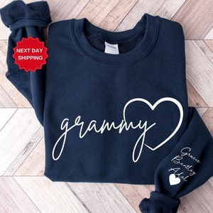 May include: Navy blue sweatshirt with the word "grammy" written in white cursive with a white heart. The sleeve has the names "Gracie Bentley Adel" written in white with a small white heart.