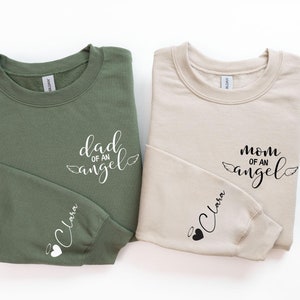 May include: Two sweatshirts, one green and one beige, with the text "dad of an angel" and "mom of an angel" on the front and the name "Clara" on the sleeve.