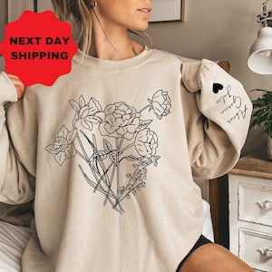 May include: A beige sweatshirt with a black line drawing of flowers on the front. The sleeve has the text "Alice, Grown, True" written in black.