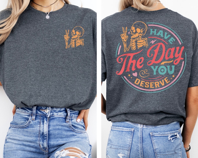 May include: A dark gray t-shirt with a skeleton graphic on the front and the text "Have the Day You Deserve" in a circle on the back. The text is in a colorful retro font.