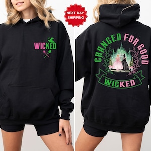 May include: Black hoodie with the word "WICKED" in pink and green, a witch hat, and a magic wand graphic. The back features the phrase "CHANGED FOR GOOD" and a scene with two characters and the word "WICKED".