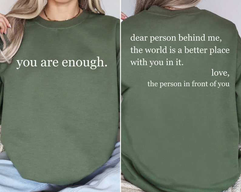 Puede incluir: Una sudadera verde con el texto "you are enough." en la parte delantera y el texto "dear person behind me, the world is a better place with you in it. love, the person in front of you" en la parte trasera.