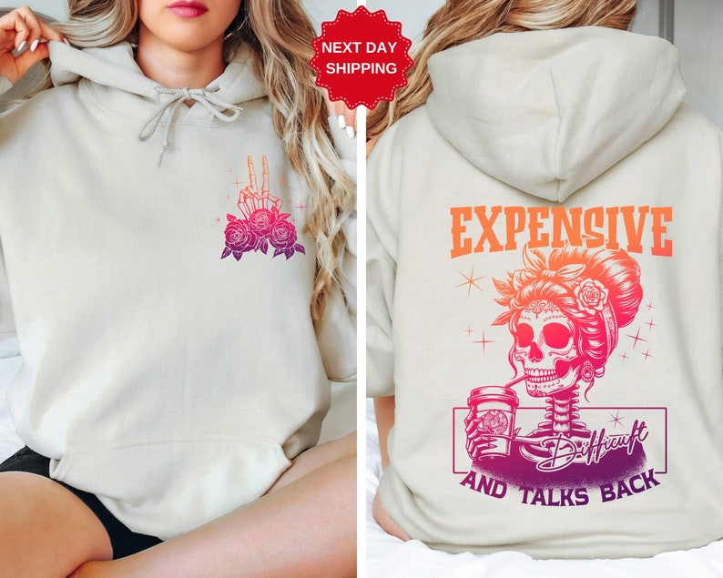May include: A light beige hoodie with a graphic of a skeleton holding a coffee cup and the text "Expensive and Talks Back" on the back. The front of the hoodie has a graphic of a skeleton hand with roses.
