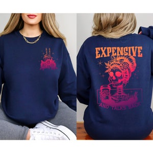 May include: Navy blue sweatshirt with a pink and orange graphic of a skeleton woman drinking coffee with the text "Expensive and Talks Back".