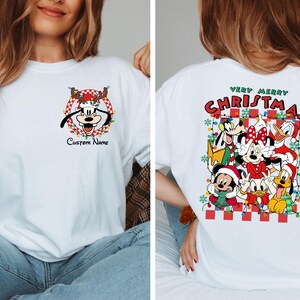 Op de afbeelding: Wit T-shirt met een kerstontwerp met Mickey Mouse, Minnie Mouse, Goofy, Donald Duck en Pluto. De tekst "Very Merry Christmas" staat op de achterkant van het shirt.