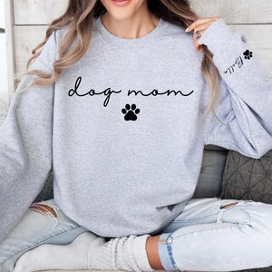 May include: Gray sweatshirt with the text "dog mom" in black cursive lettering and a black paw print. The sleeve has a black paw print and the text "Bella" in black cursive lettering.
