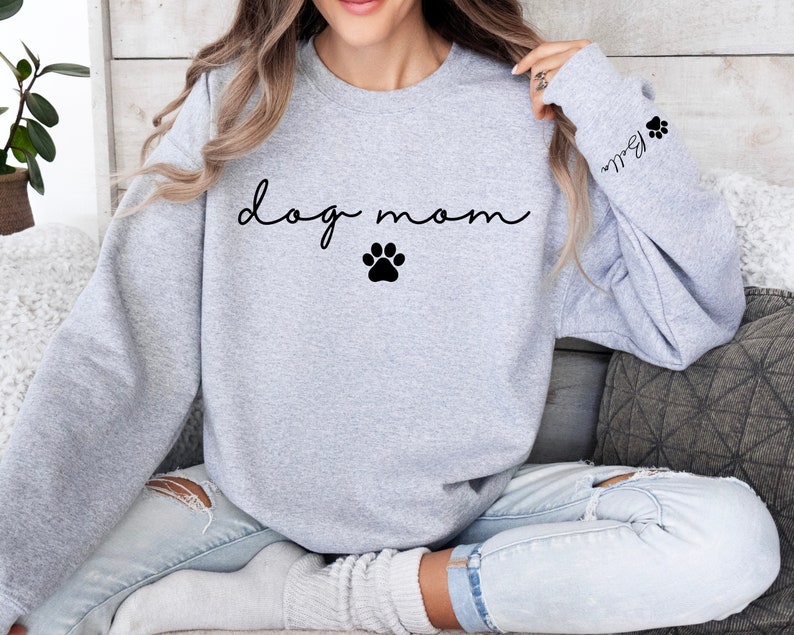 May include: Gray sweatshirt with the text "dog mom" in black cursive lettering and a black paw print. The sleeve has a black paw print and the text "Bella" in black cursive lettering.