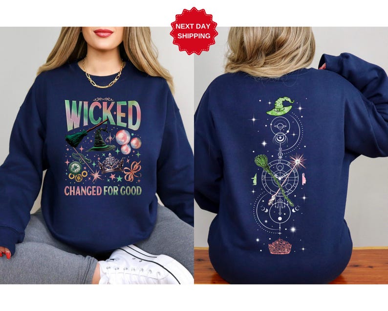 Puede incluir: Sudadera azul marino con la palabra "WICKED" en una fuente colorida y degradada. La parte delantera presenta un sombrero de bruja, una escoba y otros elementos m&aacute;gicos. La parte trasera tiene un sombrero de bruja, una escoba y un dise&ntilde;o celestial. El texto "CHANGED FOR GOOD" tambi&eacute;n est&aacute; en la parte delantera.