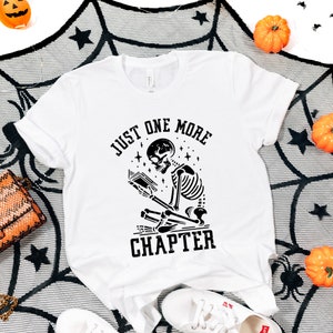 May include: White t-shirt with a black skeleton reading a book and the text "Just One More Chapter".