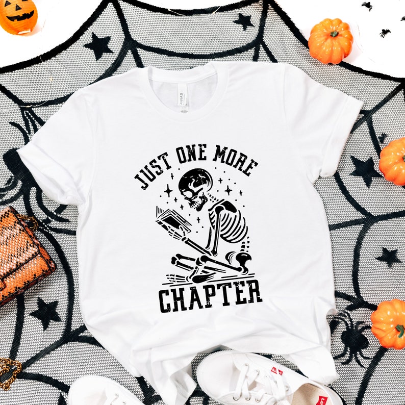 May include: White t-shirt with a black skeleton reading a book and the text "Just One More Chapter".