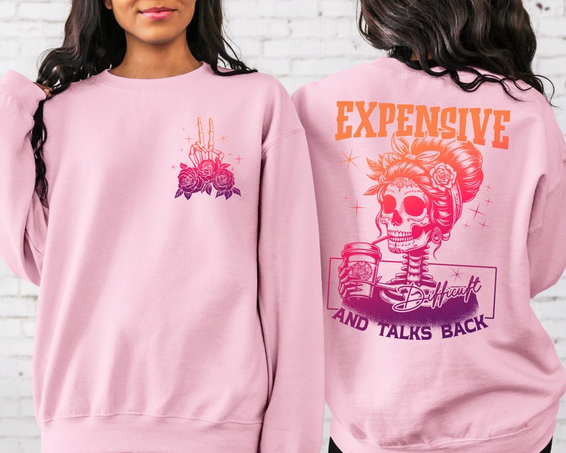 May include: Pink sweatshirt with a graphic of a skeleton woman with a coffee cup and the text "Expensive and Talks Back". The skeleton woman is wearing a flower crown and has a skull face. The sweatshirt has a pink to orange ombre effect.