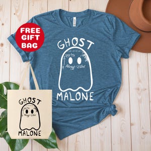 Puede incluir: Una camiseta azul con un dise&ntilde;o de fantasma blanco que dice "Ghost Malone" y tiene las palabras "Stay Away Always Tired" dentro del fantasma. La camiseta se combina con una bolsa de tela blanca con el mismo dise&ntilde;o.