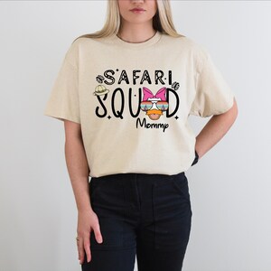 K&ouml;nnte beinhalten: Beiges T-Shirt mit dem schwarzen Aufdruck "SAFARI SQUAD Mommy", verziert mit einem Safarihut und Sonnenbrillen-Grafik. Das Shirt ist ein l&auml;ssiger Stil mit kurzen &Auml;rmeln.