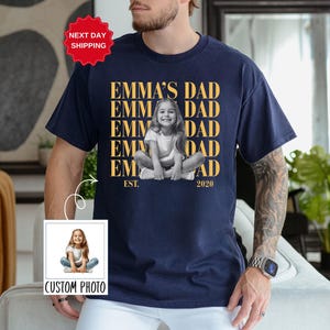 Puede incluir: Camiseta azul marino con una foto personalizada de un ni&ntilde;o y el texto "EMMA'S DAD" repetido verticalmente. La camiseta tambi&eacute;n incluye el texto "EST. 2020" y una pegatina de "NEXT DAY SHIPPING".