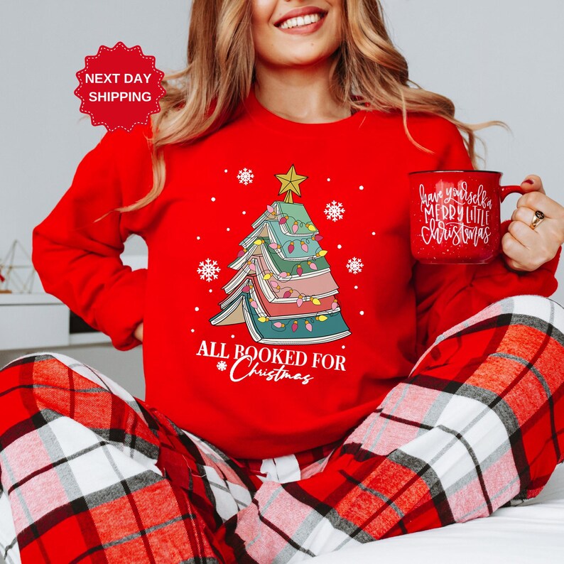 Puede incluir: Su&eacute;ter rojo de Navidad con un &aacute;rbol de Navidad en forma de libro y el texto "All Booked for Christmas".