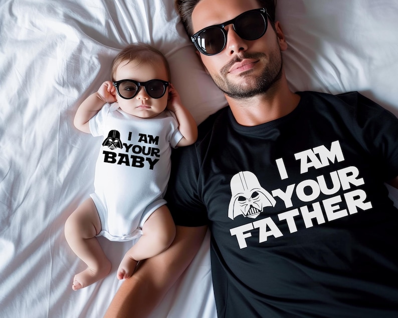 May include: A black t-shirt with the text "I AM YOUR FATHER" and a white Darth Vader graphic, next to a baby in a white onesie with the text "I AM YOUR BABY" and a Darth Vader graphic. Both are wearing black sunglasses.