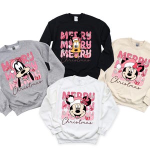 May include: Four sweatshirts with a pink and white Christmas theme. The sweatshirts feature Mickey Mouse, Minnie Mouse, and Goofy. The text on the sweatshirts reads "Merry Christmas".