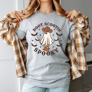 May include: A gray long-sleeved shirt with a white ghost wearing a cowboy hat and boots. The text "BOOT SCOOTIN' SPOOKY" is printed on the shirt.