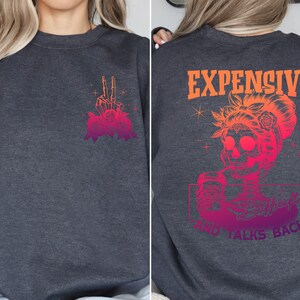May include: Gray sweatshirt with a skeleton hand with roses on the left side and the text "EXPENSIVE AND TALKS BACK" with a skeleton woman holding a drink on the right side.