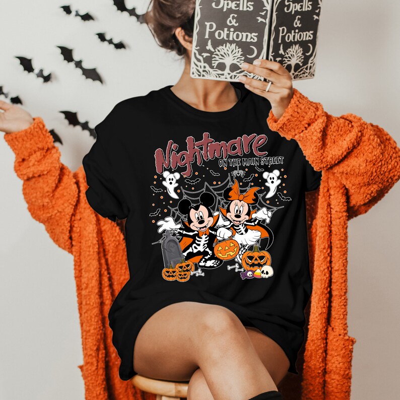 May include: Black t-shirt featuring a graphic of Mickey and Minnie Mouse dressed as skeletons for Halloween. The text "Nightmare on the Main Street" is printed on the shirt.