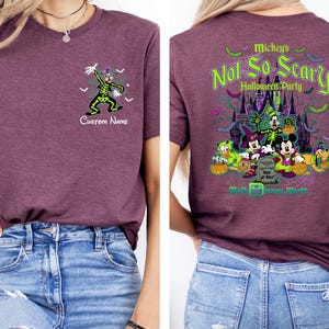 K&ouml;nnte beinhalten: Burgunderfarbenes T-Shirt mit Halloween-Design. Auf der Vorderseite des Shirts befindet sich eine Cartoonfigur in einem gr&uuml;n-schwarzen Kost&uuml;m mit dem Text "Custom Name". Auf der R&uuml;ckseite des Shirts befindet sich eine Grafik von Mickey's Not So Scary Halloween Party.