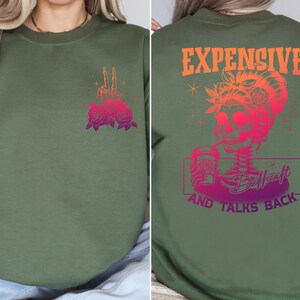 May include: Green sweatshirt with a pink and purple graphic of a skull holding a coffee cup and the text "Expensive and Talks Back". The front of the sweatshirt has a pink and purple graphic of a hand with roses.