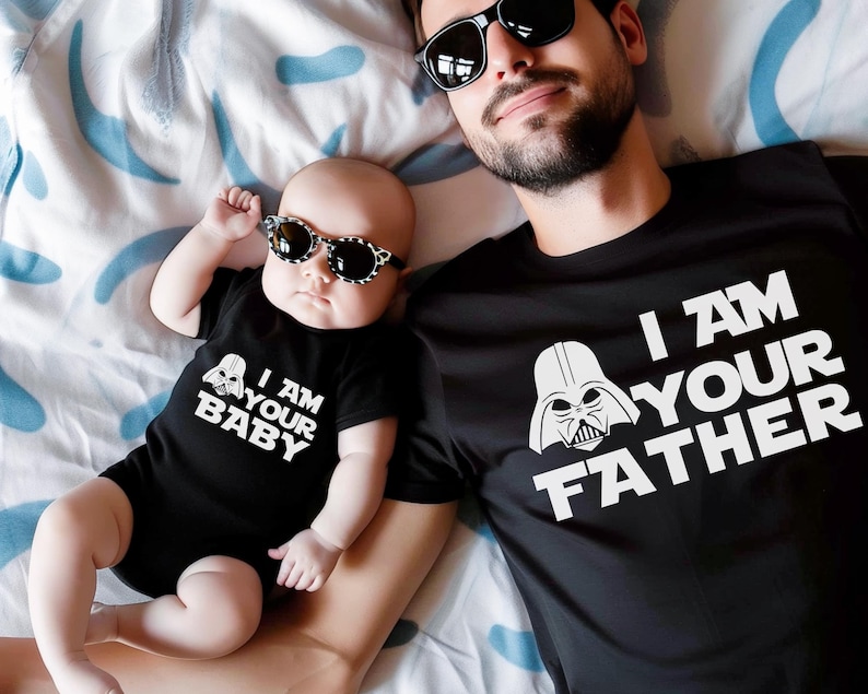 May include: A black t-shirt with the text "I AM YOUR FATHER" and a Darth Vader graphic, next to a baby wearing a black onesie with the text "I AM YOUR BABY" and a Darth Vader graphic. Both are wearing sunglasses.