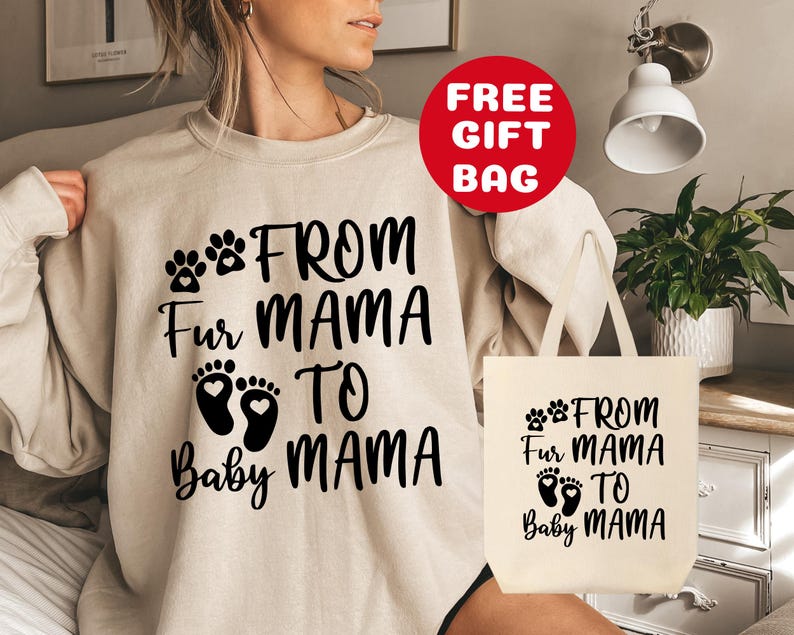 May include: A beige sweatshirt with black text that reads "From Fur Mama to Baby Mama" and two paw prints. A beige tote bag with the same text and paw prints is also shown.
