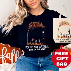 Op de afbeelding: Zwart sweatshirt met een afbeelding van Jack Skellington en Sally uit The Nightmare Before Christmas die door een herfstsc&egrave;ne lopen. De tekst "It's the most wonderful time of the year" staat op het sweatshirt gedrukt. Een gratis tote bag is inbegrepen.