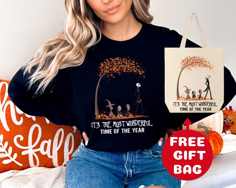 Op de afbeelding: Zwart sweatshirt met een afbeelding van Jack Skellington en Sally uit The Nightmare Before Christmas die door een herfstsc&egrave;ne lopen. De tekst "It's the most wonderful time of the year" staat op het sweatshirt gedrukt. Een gratis tote bag is inbegrepen.