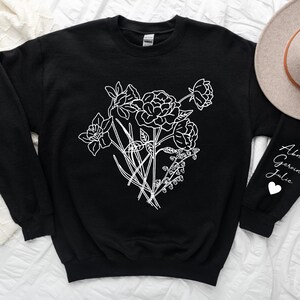 May include: Black sweatshirt with a white outline of a bouquet of flowers on the front. The left sleeve has the names "Abner, Gerwin, Julie" written in white with a white heart symbol.