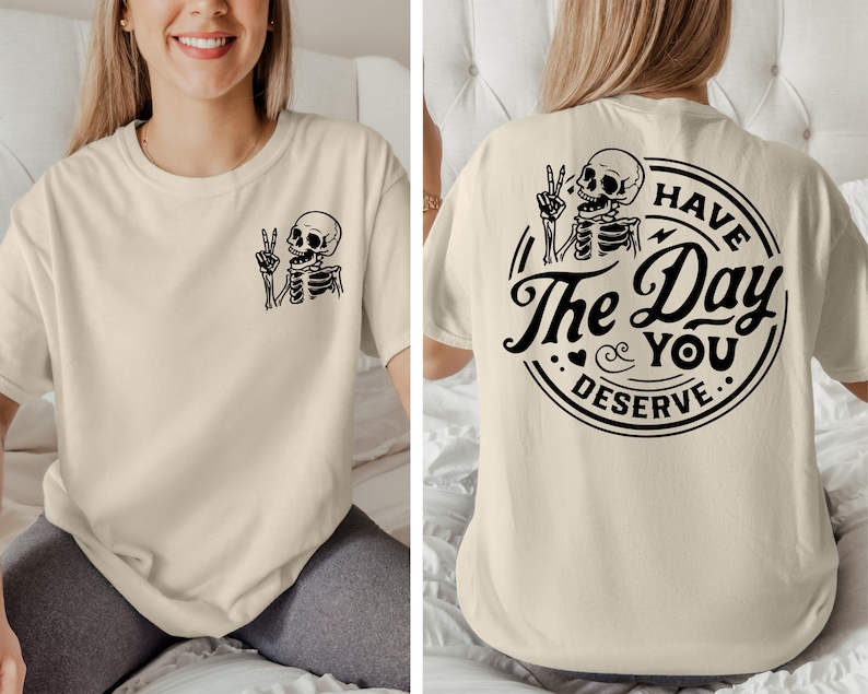 May include: A beige t-shirt with a skeleton graphic on the front and the text "Have The Day You Deserve" with a skeleton graphic on the back.
