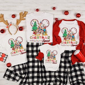 May include: A family matching Christmas pajama set with a white t-shirt featuring a Mickey Mouse ear design with a Christmas tree and characters from Disney World. The text "Christmas Squad" is printed on the shirt. The pajamas are black and white plaid.