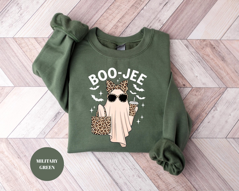 May include: Military green sweatshirt with the text "BOO-JEE" and a graphic of a ghost wearing sunglasses and a leopard print bow, holding a purse and a coffee cup. The design includes bats and stars.