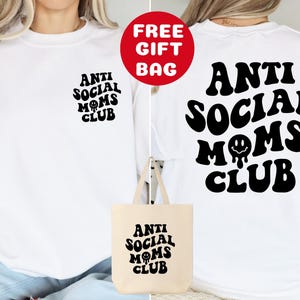 May include: White long-sleeve sweatshirt with black text that reads "Anti Social Moms Club" with a smiley face. A white tote bag with the same text and design is included.
