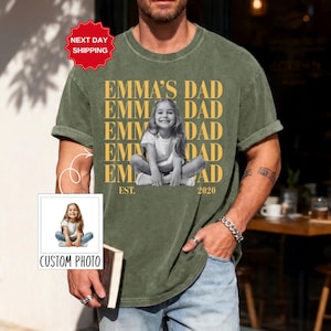 Puede incluir: Camiseta verde oliva con el texto "EMMA'S DAD" repetido verticalmente y una foto en blanco y negro de una ni&ntilde;a. La camiseta tambi&eacute;n tiene el texto "EST. 2020". Una peque&ntilde;a imagen con el texto "CUSTOM PHOTO" est&aacute; en la esquina inferior izquierda.